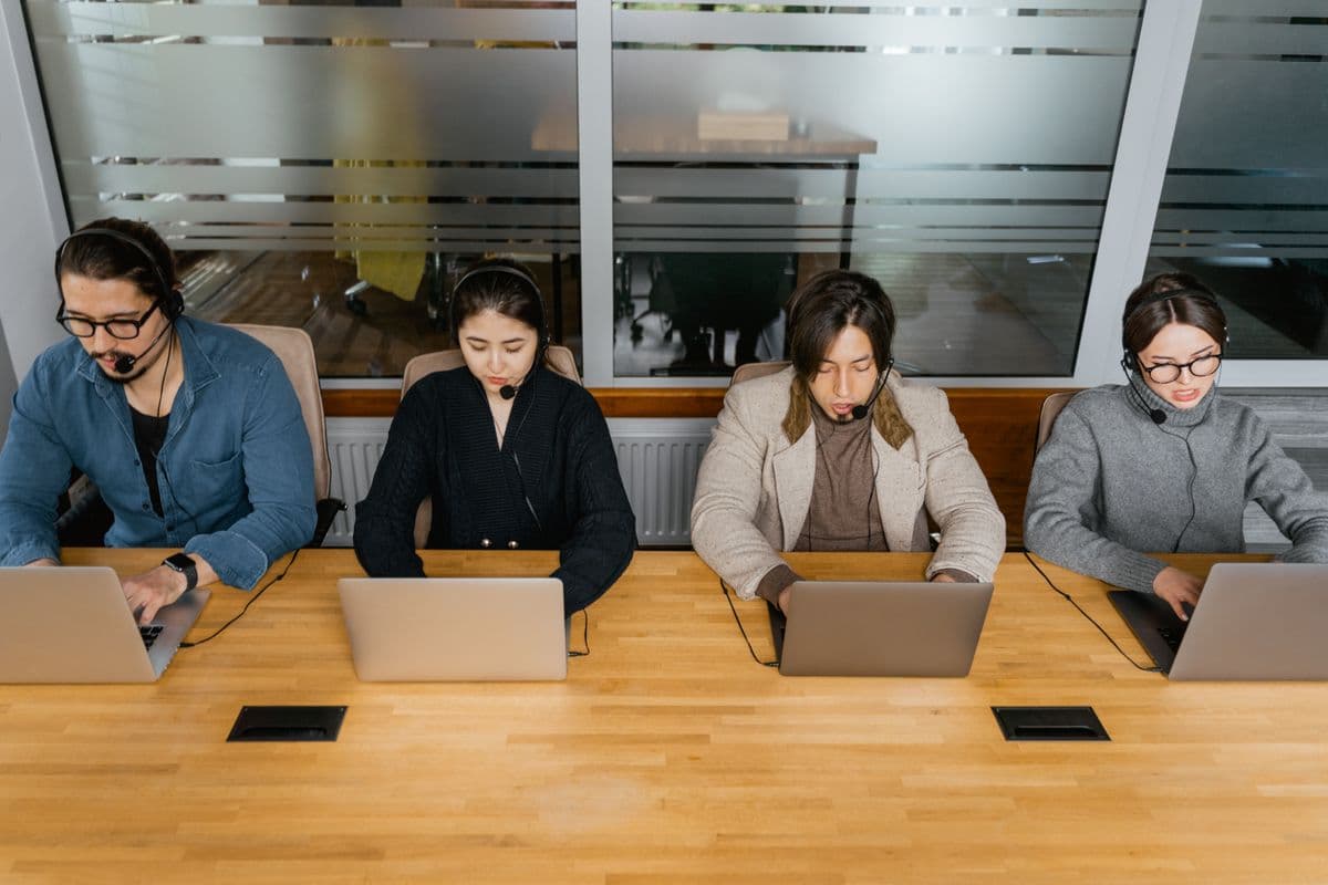 Support specialists working with laptops and headsets around a shared desk